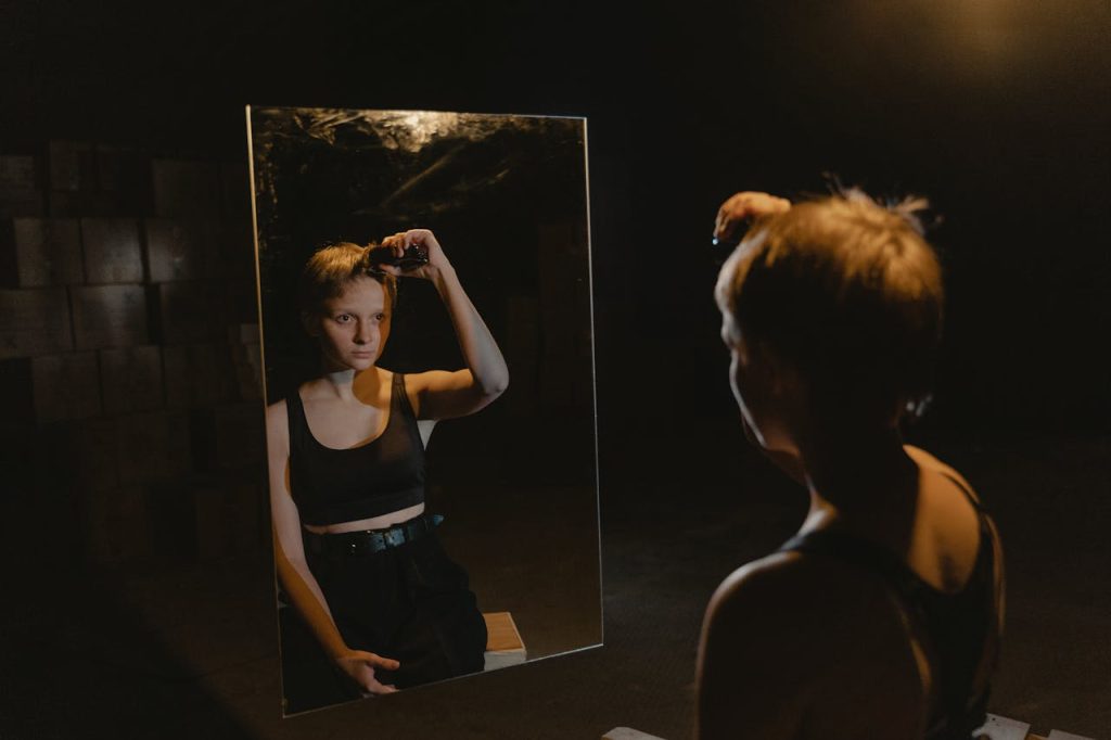 A person looks into a mirror while grooming in a dimly lit space, creating a contemplative mood.