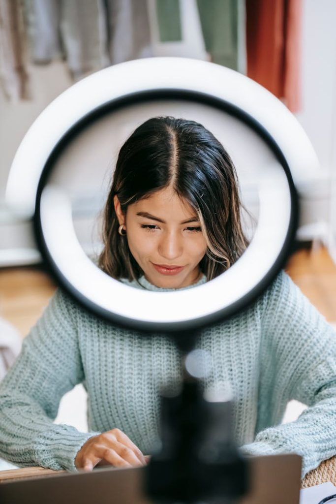Hispanic woman focused on laptop work with a ring light in cozy home setting.